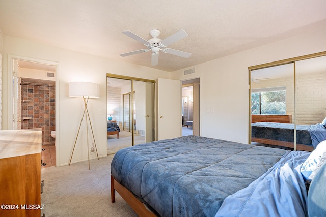 bedroom featuring a textured ceiling, light carpet, a ceiling fan, visible vents, and multiple closets