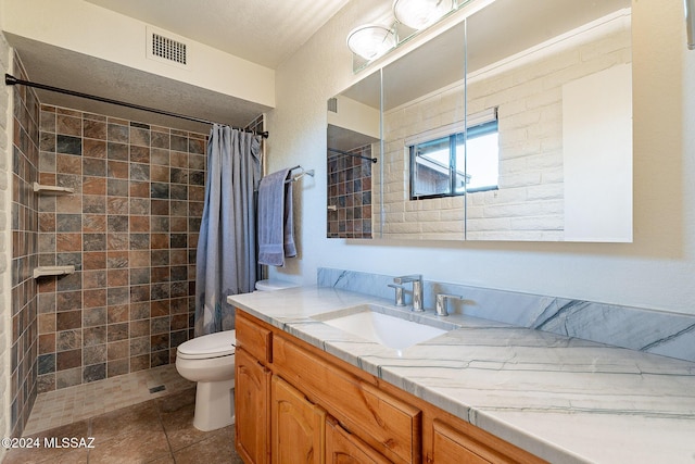 bathroom with visible vents, toilet, vanity, tiled shower, and tile patterned floors