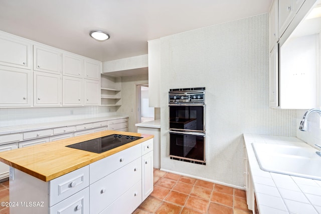 kitchen with black appliances, a kitchen island, sink, white cabinets, and tile countertops