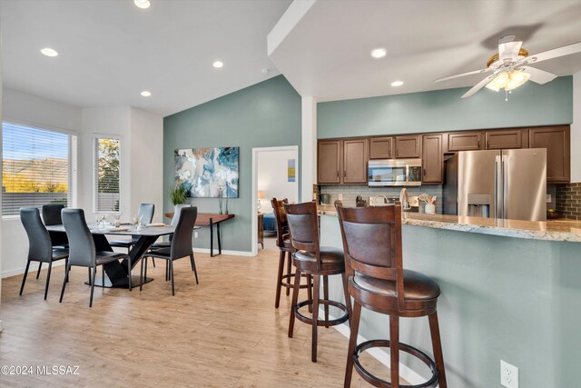 kitchen with light wood-type flooring, stainless steel appliances, lofted ceiling, and decorative backsplash