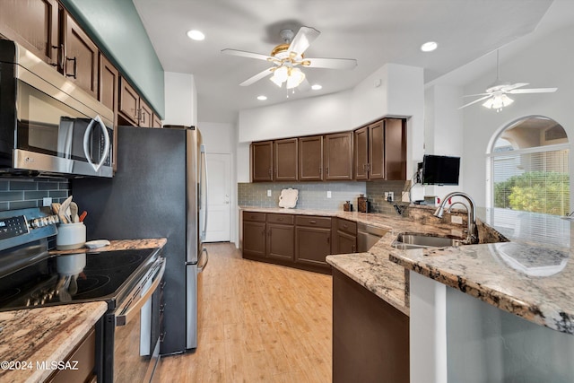 kitchen with stainless steel appliances, light stone counters, decorative backsplash, sink, and light wood-type flooring