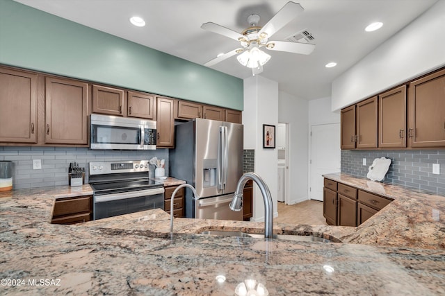 kitchen with backsplash, appliances with stainless steel finishes, light stone countertops, sink, and ceiling fan