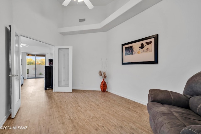 living area featuring a high ceiling, ceiling fan, and light wood-type flooring