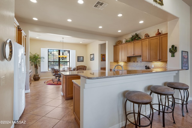 kitchen with kitchen peninsula, light tile patterned floors, pendant lighting, decorative backsplash, and a chandelier