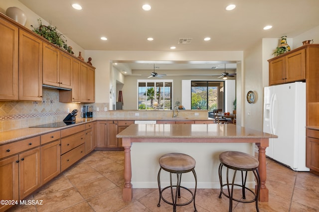 kitchen featuring kitchen peninsula, white refrigerator with ice dispenser, a kitchen breakfast bar, a kitchen island, and backsplash