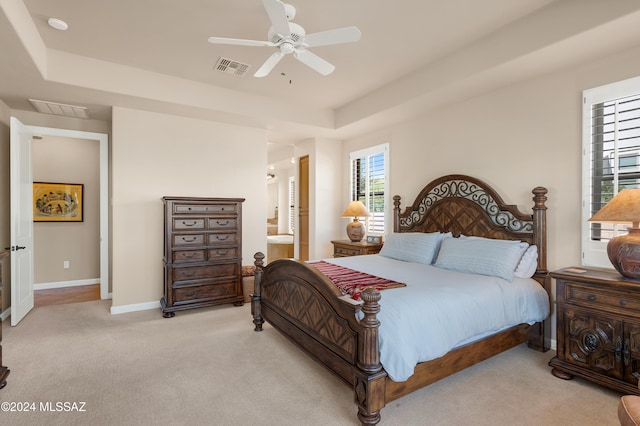 carpeted bedroom with a tray ceiling, ceiling fan, and ensuite bathroom