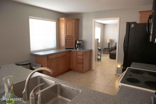 kitchen with light tile patterned floors, stove, black fridge, and sink