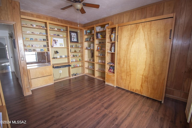 unfurnished office with dark wood-type flooring, wooden walls, ceiling fan, built in features, and a textured ceiling