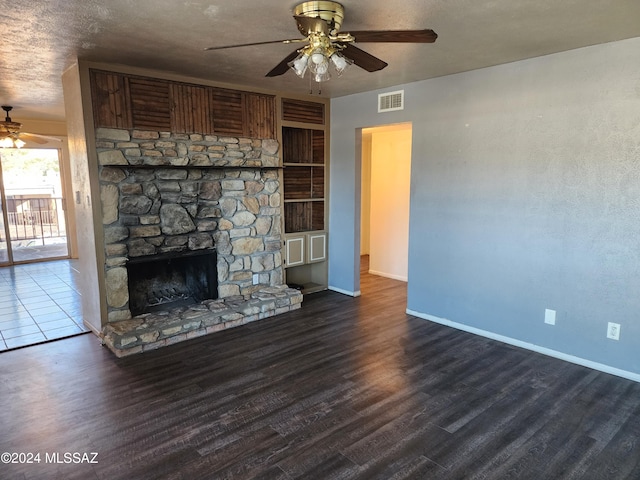 unfurnished living room featuring ceiling fan, a fireplace, dark wood-type flooring, and a textured ceiling