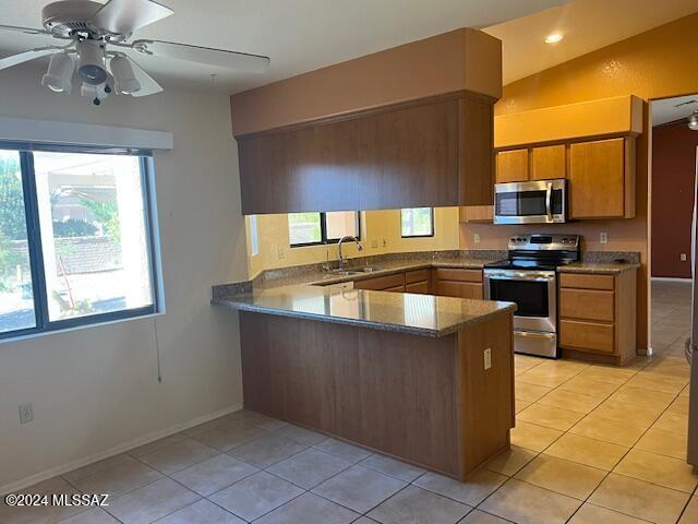 kitchen with appliances with stainless steel finishes, lofted ceiling, sink, kitchen peninsula, and light tile patterned floors