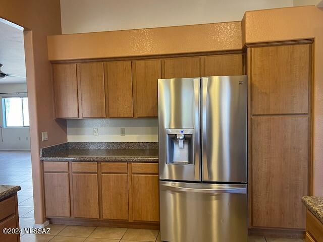 kitchen with ceiling fan, light tile patterned floors, stainless steel fridge, and dark stone counters