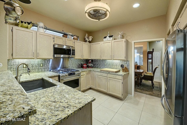 kitchen with appliances with stainless steel finishes, backsplash, light stone counters, sink, and light tile patterned flooring