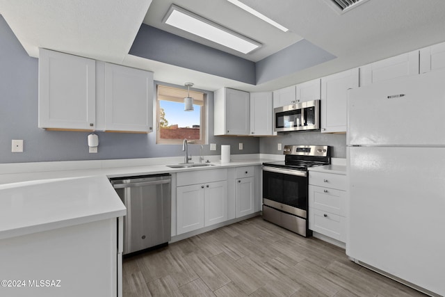 kitchen featuring sink, white cabinetry, light wood-type flooring, appliances with stainless steel finishes, and decorative light fixtures