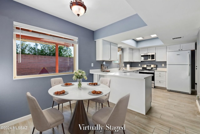 kitchen with kitchen peninsula, appliances with stainless steel finishes, light hardwood / wood-style floors, and white cabinets