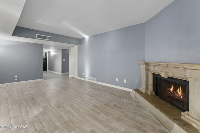 unfurnished living room featuring a stone fireplace and light wood-type flooring