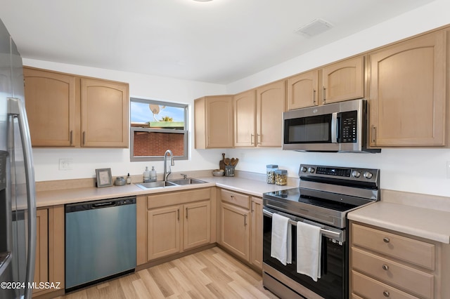 kitchen with sink, light wood-type flooring, light brown cabinets, and appliances with stainless steel finishes