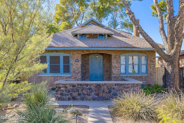 view of front of property featuring a shingled roof, brick siding, and fence