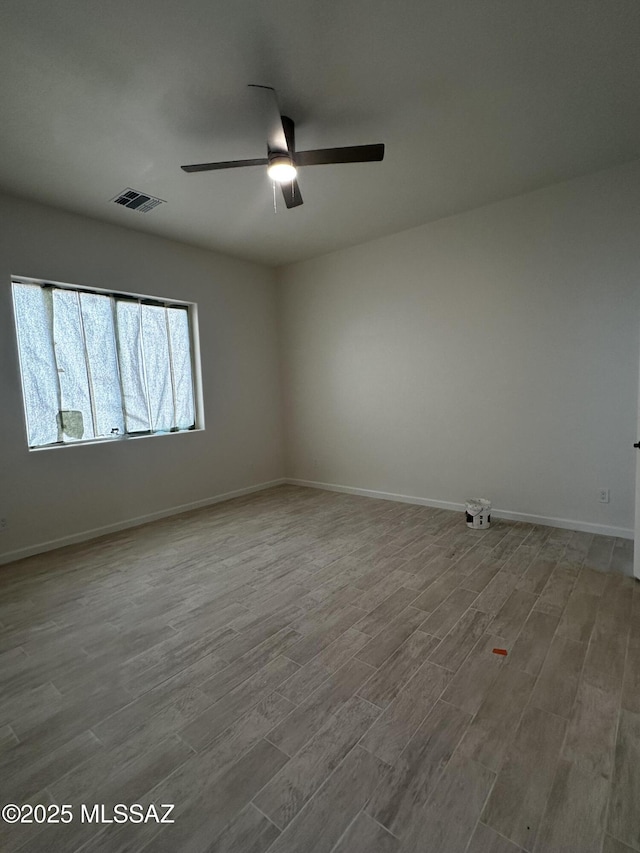 empty room with a ceiling fan, wood finished floors, visible vents, and baseboards