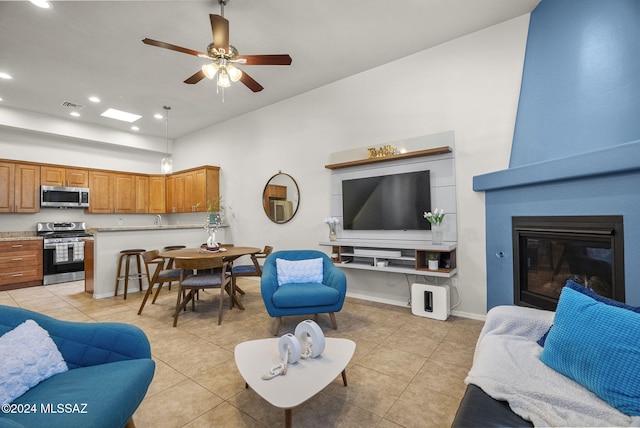 living room with light tile patterned flooring, sink, a large fireplace, and ceiling fan