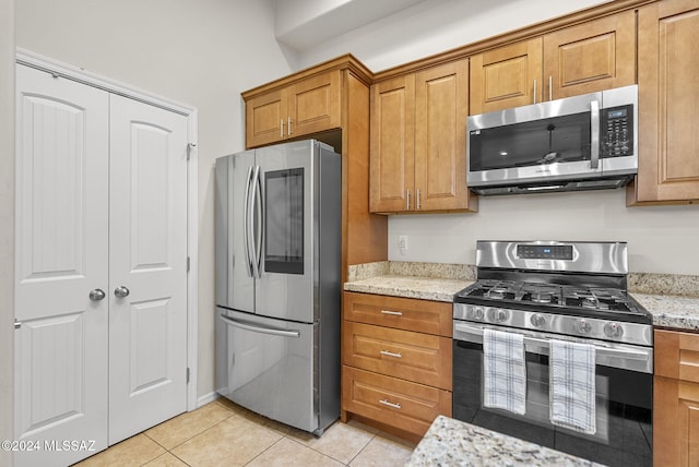 kitchen with appliances with stainless steel finishes, light tile patterned floors, and light stone counters
