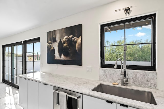 kitchen featuring white cabinets, dishwasher, light stone countertops, and sink