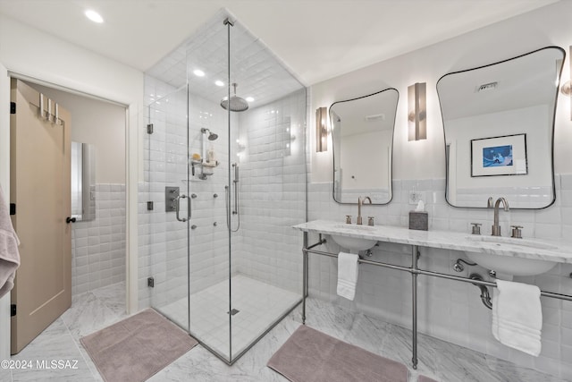 bathroom with an enclosed shower, tile walls, and dual sinks