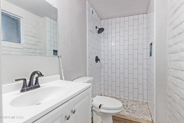 bathroom with a tile shower, vanity, and toilet