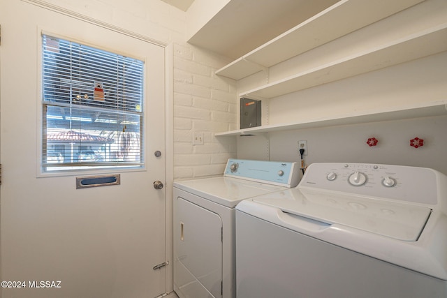 laundry area featuring electric panel, separate washer and dryer, and brick wall