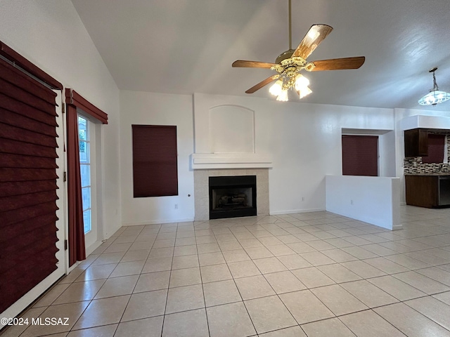 unfurnished living room with vaulted ceiling, a tiled fireplace, light tile patterned flooring, and ceiling fan with notable chandelier