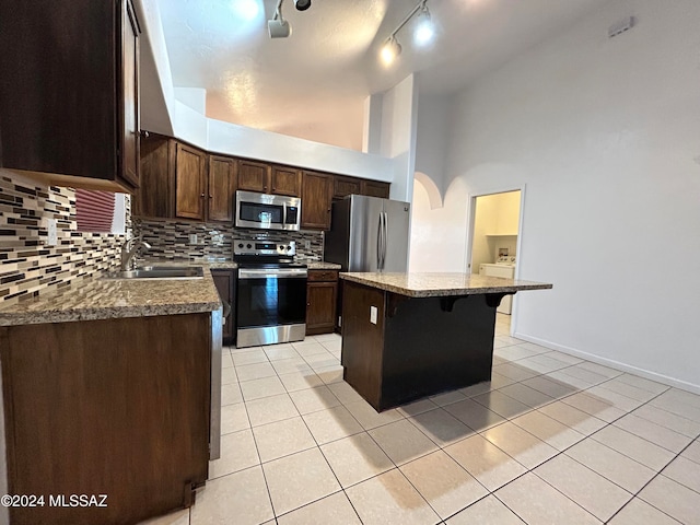 kitchen with sink, stainless steel appliances, light tile patterned floors, a kitchen breakfast bar, and a kitchen island