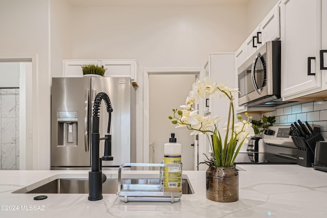 kitchen featuring decorative backsplash, stove, white cabinetry, and light stone counters