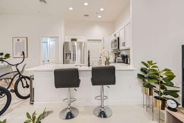 kitchen featuring a kitchen bar, stainless steel appliances, white cabinets, kitchen peninsula, and tasteful backsplash