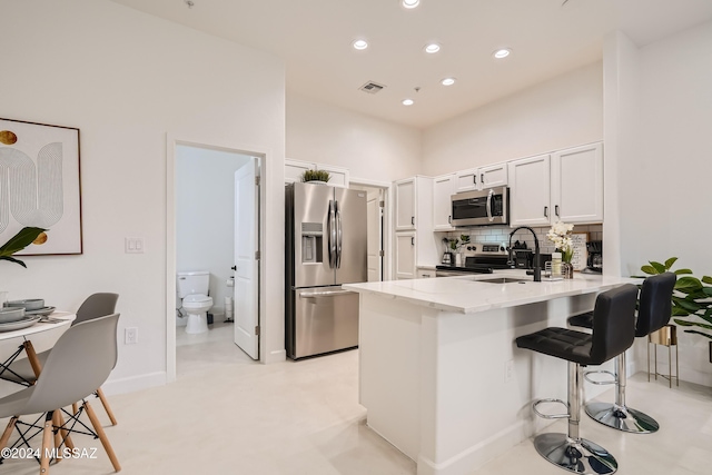 kitchen featuring sink, kitchen peninsula, appliances with stainless steel finishes, a kitchen bar, and white cabinets