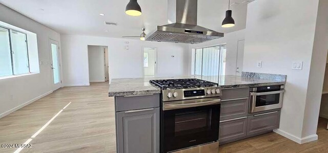 kitchen with stainless steel appliances, light stone countertops, island range hood, light hardwood / wood-style flooring, and pendant lighting