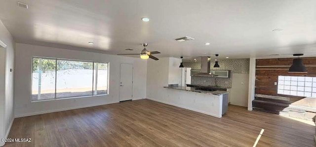 kitchen featuring kitchen peninsula, wood-type flooring, white cabinets, wall chimney range hood, and decorative backsplash