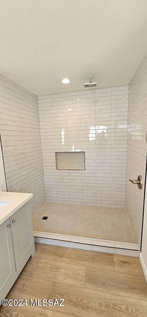 bathroom with hardwood / wood-style floors, tiled shower, and vanity