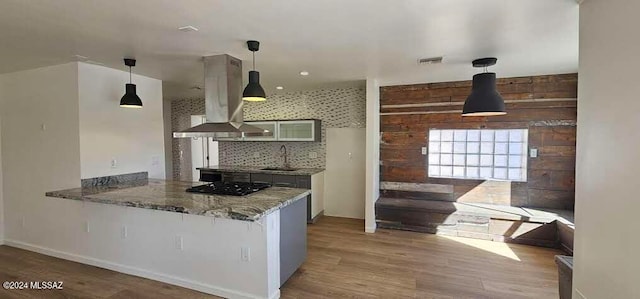 kitchen with island exhaust hood, light stone countertops, sink, hardwood / wood-style flooring, and kitchen peninsula