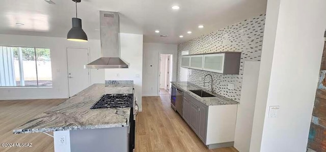 kitchen featuring stainless steel appliances, sink, light stone countertops, wall chimney exhaust hood, and hanging light fixtures