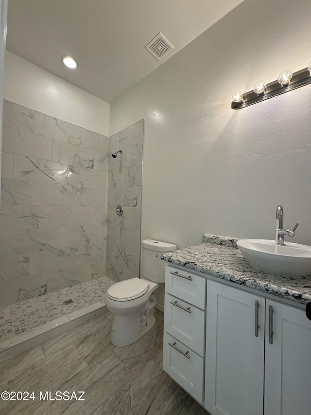 bathroom featuring toilet, a tile shower, and vanity