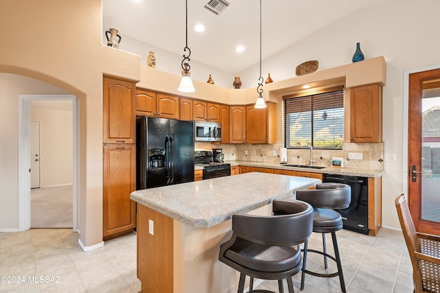 kitchen with a kitchen breakfast bar, sink, black appliances, decorative light fixtures, and a kitchen island