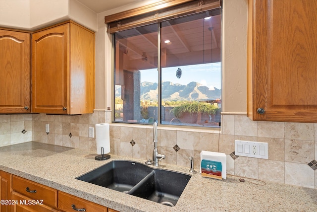 kitchen with backsplash, a mountain view, light stone countertops, and sink