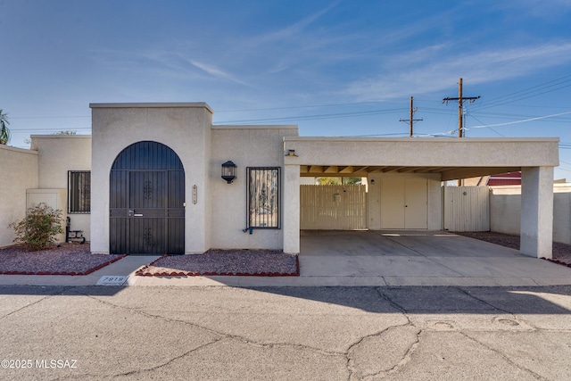 view of front of property featuring an attached carport, fence, a gate, and stucco siding