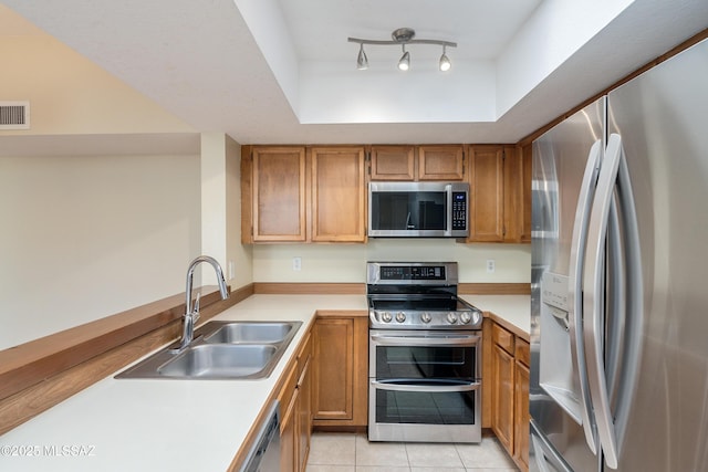 kitchen with a raised ceiling, appliances with stainless steel finishes, a sink, and light countertops