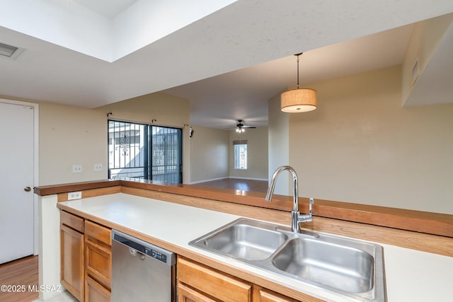 kitchen featuring brown cabinetry, hanging light fixtures, light countertops, stainless steel dishwasher, and a sink