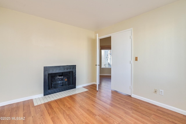 unfurnished living room featuring light wood-style floors, baseboards, and a fireplace with flush hearth