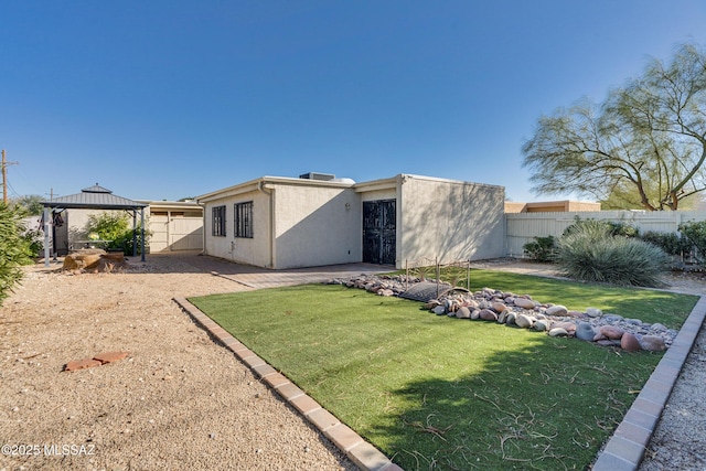 rear view of property with a fenced backyard, a yard, a gazebo, and stucco siding