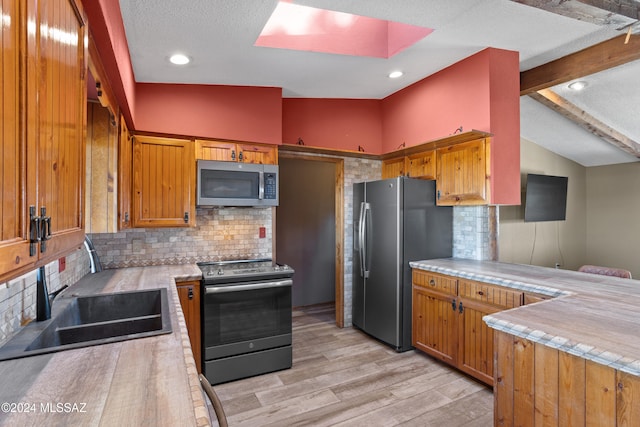 kitchen featuring light hardwood / wood-style flooring, sink, decorative backsplash, appliances with stainless steel finishes, and a skylight