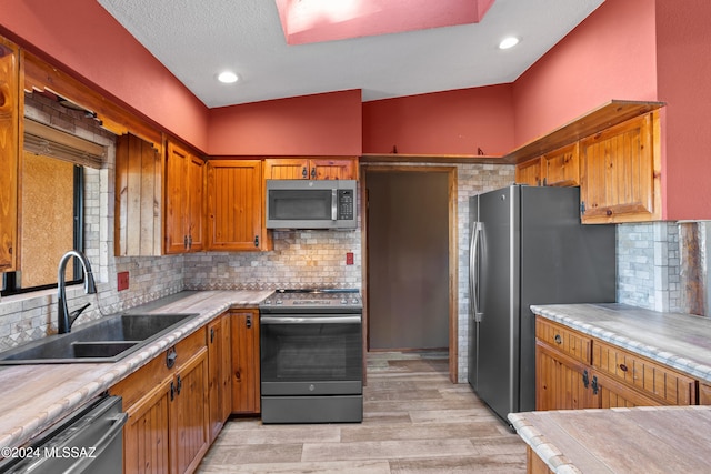 kitchen featuring tasteful backsplash, stainless steel appliances, vaulted ceiling, sink, and light hardwood / wood-style floors