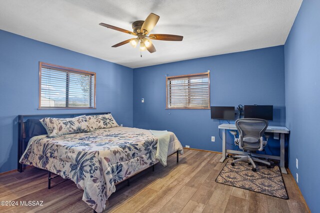 bedroom with ceiling fan, wood-type flooring, and a textured ceiling