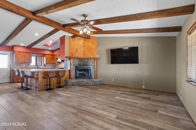 unfurnished living room featuring a fireplace, vaulted ceiling with beams, ceiling fan, and light wood-type flooring